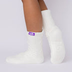 The Foozie™ Move in White, side view with one heel raised, showing the diamond cable knit and the logo tab